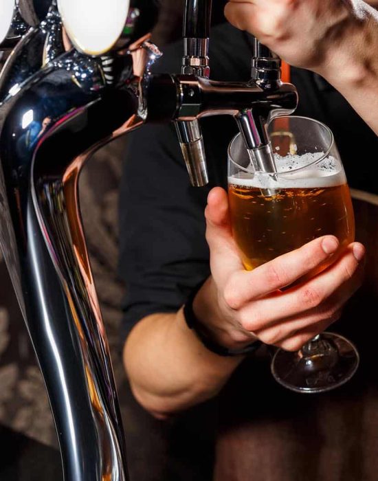 The bartender pours the beer into the glass from the beer tap